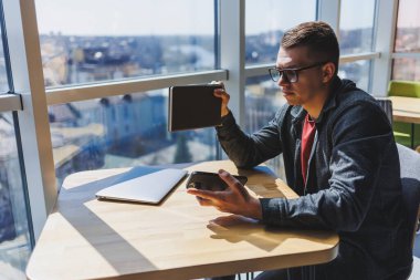 Gözlüklü neşeli serbest çalışan akıllı telefonlu ve gülümseyen gün boyunca kafede dizüstü bilgisayarlı ve not defterli bir masada oturuyor. Ofisten uzakta çalışıyor..