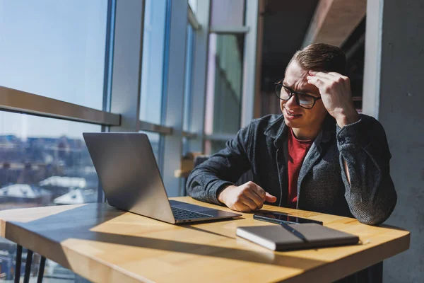 Freelancer Brýlích Podívá Notebooku Naštvaný Zatímco Sedí Stolu Notebookem Poznámkovým — Stock fotografie