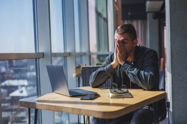 Modern bir dizüstü bilgisayarla uzaktan çalışan, mola sırasında masaya oturup kameraya gülümseyen, vizyon düzeltme gözlüklü mutlu bir insan programcı portresi.