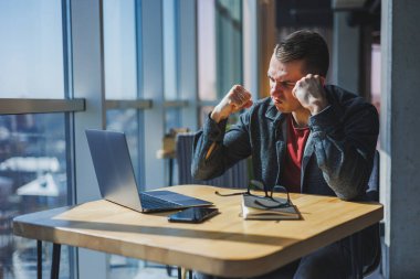 Modern bir dizüstü bilgisayarla uzaktan çalışan, mola sırasında masaya oturup kameraya gülümseyen, vizyon düzeltme gözlüklü mutlu bir insan programcı portresi.