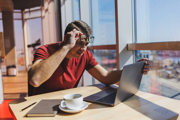 Smart software developer sitting at desktop in coworking space with laptop and creating publishing idea, using netbook for messaging and networking during freelance work