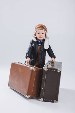 Kasklı ve pilot ceketli mutlu bir çocuk kahverengi bir bavul taşıyor. Bir çocuk pilotun portresi, deri ceketli bir çocuk. Bavullu küçük gezgin.