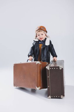 Kasklı ve pilot ceketli mutlu bir çocuk kahverengi bir bavul taşıyor. Bir çocuk pilotun portresi, deri ceketli bir çocuk. Bavullu küçük gezgin.