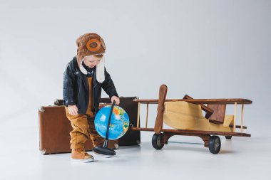 Deri ceketli ve pilot şapkalı bir çocuk, tahta bir uçak, bir küre, kahverengi bavullar. Çocukların tahta oyuncakları.
