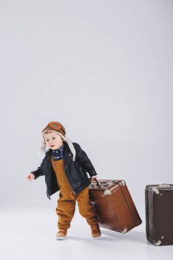 Kasklı ve pilot ceketli mutlu bir çocuk kahverengi bir bavul taşıyor. Bir çocuk pilotun portresi, deri ceketli bir çocuk. Bavullu küçük gezgin.