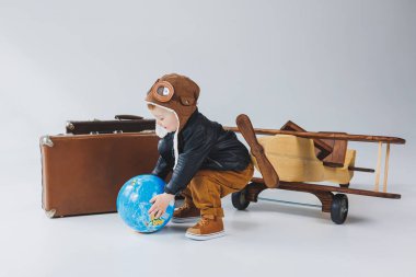 Deri ceketli ve pilot şapkalı bir çocuk, tahta bir uçak, bir küre, kahverengi bavullar. Çocukların tahta oyuncakları.