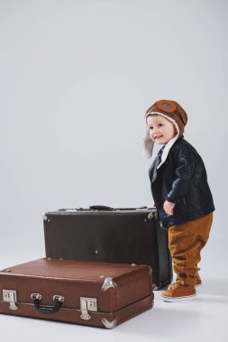 Kasklı ve pilot ceketli mutlu bir çocuk kahverengi bir bavul taşıyor. Bir çocuk pilotun portresi, deri ceketli bir çocuk. Bavullu küçük gezgin.
