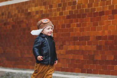 Üç yaşında, deri ceketli ve kahverengi pantolonlu şık bir çocuk sokakta yürüyor. Modern çocuk. Çocuk modası. Mutlu çocuk