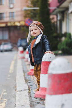 Üç yaşında, deri ceketli ve kahverengi pantolonlu şık bir çocuk sokakta yürüyor. Modern çocuk. Çocuk modası. Mutlu çocuk