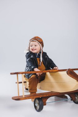 Küçük bir çocuk ahşap bir uçakta oturuyor. Çevre dostu çocuk oyuncakları. Deri ceketli ve şapkalı çocuk.