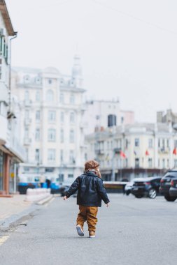 Üç yaşında, deri ceketli ve kahverengi pantolonlu şık bir çocuk sokakta yürüyor. Modern çocuk. Çocuk modası. Mutlu çocuk