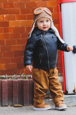 Üç yaşında, deri ceketli ve kahverengi pantolonlu şık bir çocuk sokakta yürüyor. Modern çocuk. Çocuk modası. Mutlu çocuk