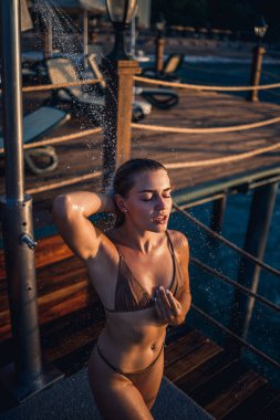 Güzel genç bir kadın açık denizde güneşli bir günde mayoyla rahatlatıcı bir duş alır. Tatildeki kız dinleniyor. Seçici odak