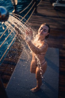 Güzel genç bir kadın açık denizde güneşli bir günde mayoyla rahatlatıcı bir duş alır. Tatildeki kız dinleniyor. Seçici odak