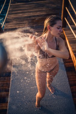 Güzel genç bir kadın açık denizde güneşli bir günde mayoyla rahatlatıcı bir duş alır. Tatildeki kız dinleniyor. Seçici odak