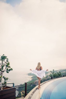 Siyah mayolu güzel bir kadın açık havuz kenarında deniz manzaralı poz veriyor.