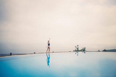 Siyah mayolu güzel bir kadın açık havuz kenarında deniz manzaralı poz veriyor.