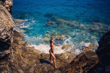 Mayo giymiş genç bir kadın Akdeniz 'in kayalık bir sahilinde duruyor. Deniz eğlencesi konsepti. Seçici odak