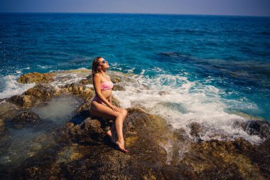 Türkiye 'de Akdeniz' in kayalık bir sahilinde mayo giymiş genç ve güzel bir kadın oturuyor. Deniz eğlencesi konsepti. Seçici odak