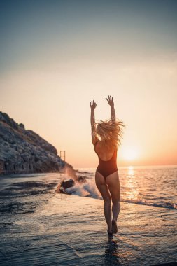 Gün batımında deniz kenarında siyah mayo giymiş güzel bir kadın. Gün batımında okyanus kıyısında dinlenen yetişkin ince bir kız. Yaz tatili kavramı. Seçici odak