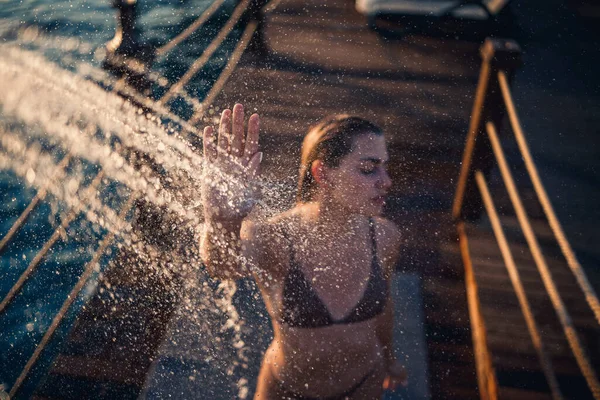 Güzel genç bir kadın açık denizde güneşli bir günde mayoyla rahatlatıcı bir duş alır. Tatildeki kız dinleniyor. Seçici odak