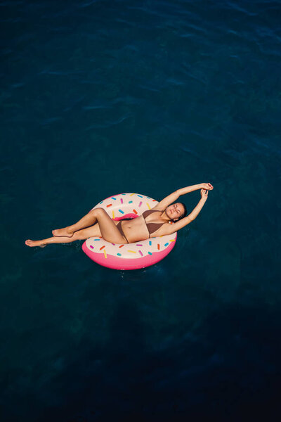 Молодая женщина в купальнике плавает на надувном кольце в море. Летние каникулы.