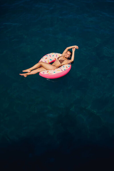 Молодая женщина в купальнике плавает на надувном кольце в море. Летние каникулы.