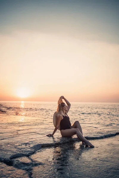 Güneş gözlüklü genç bir kadın siyah bir mayo giymiş deniz kıyısında dinleniyor. Seçici odak