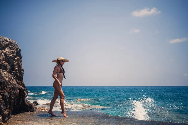 수영복을 모자를 아름다운 소녀가 바위가 해안을 다닌다 바다에 여름의 — 스톡 사진