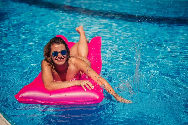Havuzdaki pembe şişme yatakta mayo giymiş seksi bir kadın yatıyor. Sıcak ve güneşli bir yaz gününde havuz kenarında rahatla. Tatil kavramı