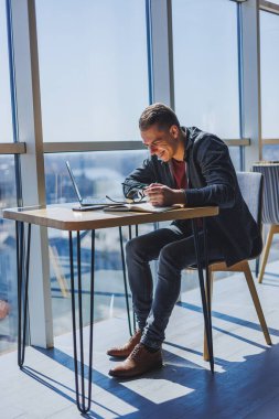Görme düzeltmesi için optik gözlüklü mutlu adam bir kafede otururken internet üzerinden kablosuz bağlantı kullanarak sosyal ağlarda komik bilgiler arıyor.
