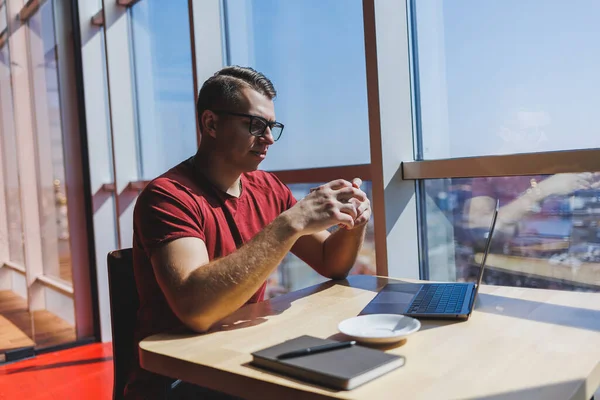 Modern bir dizüstü bilgisayarla uzaktan çalışan, mola sırasında masaya oturup kameraya gülümseyen, vizyon düzeltme gözlüklü mutlu bir insan programcı portresi.