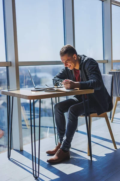 Görme düzeltmesi için optik gözlüklü mutlu adam bir kafede otururken internet üzerinden kablosuz bağlantı kullanarak sosyal ağlarda komik bilgiler arıyor.