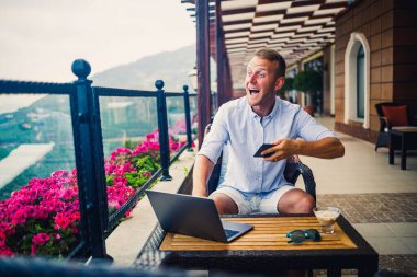 Beyaz gömlekli ve şortlu genç yakışıklı iş adamı masadaki bir kafede dizüstü bilgisayarla oturuyor. Dinlenirken çalış