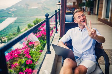 Beyaz gömlekli ve şortlu genç yakışıklı iş adamı masadaki bir kafede dizüstü bilgisayarla oturuyor. Dinlenirken çalış