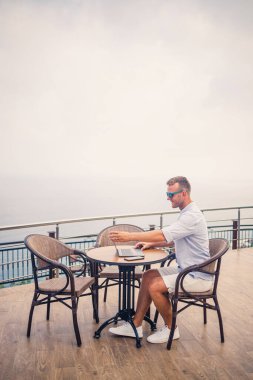 Akdeniz 'e bakan bir dizüstü bilgisayarla havuz kenarında oturan yakışıklı, genç ve başarılı bir iş adamı. Tatilde uzaktan çalışma. Tatil kavramı