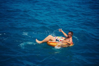 Genç bir adam güneşli bir günde şişme bir yüzükle açık denizde yüzer. Yaz tatili, tatildeki turist.