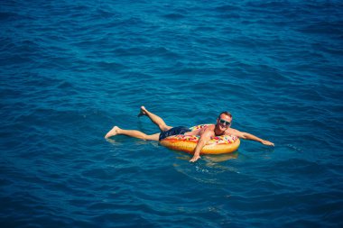 Bir adam mavi suyla şişme bir yüzüğün üzerinde yüzüyor. Güneşli bir günde deniz tatili. Türkiye tatil kavramı