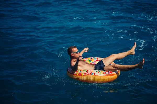 Genç bir adam güneşli bir günde şişme bir yüzükle açık denizde yüzer. Yaz tatili, tatildeki turist.