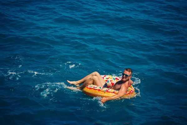 Genç bir adam güneşli bir günde şişme bir yüzükle açık denizde yüzer. Yaz tatili, tatildeki turist.