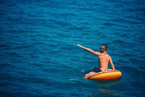Genç bir adam mavi suyla denizde şişirilebilir bir halka üzerinde yüzüyor. Güneşli bir günde güzel bir tatil. Tatil konsepti, üst görünüm.