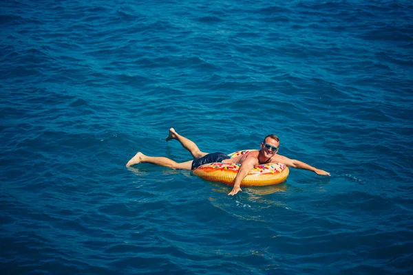Bir adam mavi suyla şişme bir yüzüğün üzerinde yüzüyor. Güneşli bir günde deniz tatili. Türkiye tatil kavramı