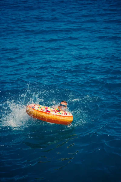 Bir adam şişme kauçuk bir çemberin üzerinde uzanır ve açık güneşli bir yaz gününde mavi denizde yüzer.