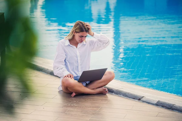 Havuz başında dizüstü bilgisayarla çalışan güzel bir kadın. Serbest uzaktan çalışma