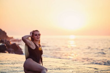 Deniz kıyısında siyah mayo giymiş güzel bir bayan, gülen surat. Altın günbatımı ışığı