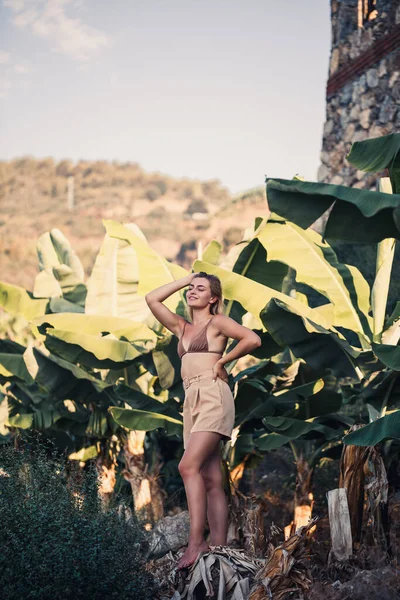 Güzel bir kız, bir palmiye ağacının yanında güzel bir poz verir. Muz tarlasında çekilen bir portre.