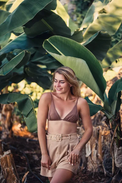 Güzel bir kız, bir palmiye ağacının yanında güzel bir poz verir. Muz tarlasında çekilen bir portre.