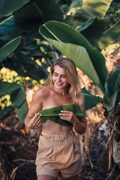 Güzel bir kız, bir palmiye ağacının yanında güzel bir poz verir. Muz tarlasında çekilen bir portre.