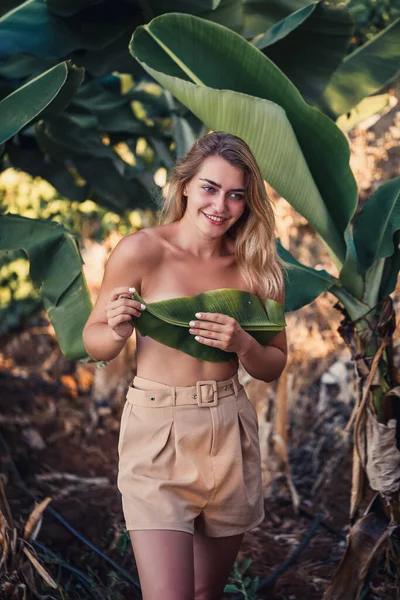 Güzel bir kız, bir palmiye ağacının yanında güzel bir poz verir. Muz tarlasında portre çekimi yapar. Seçici odak