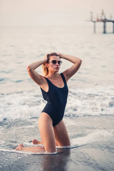 Piękna Młoda Dziewczyna Ubrana Czarny Strój Kąpielowy Klęka Piaszczystej Plaży — Zdjęcie stockowe